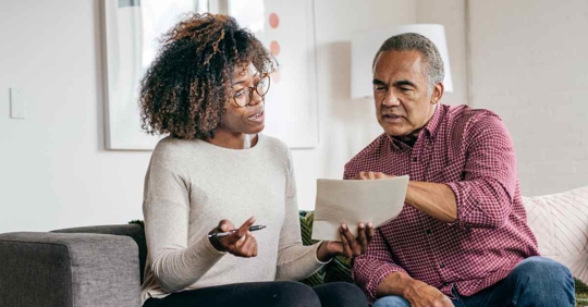 A man and woman reviewing documents while sitting on their couch