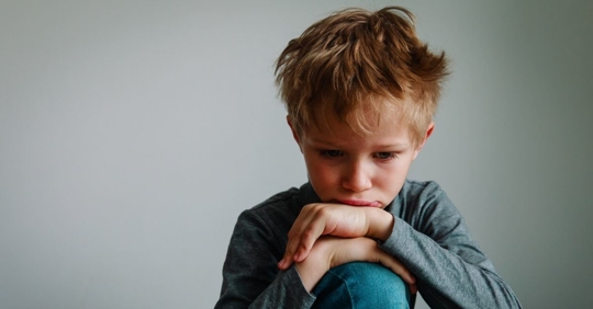 A young boy looking upset about something. He is resting his head on his hands.