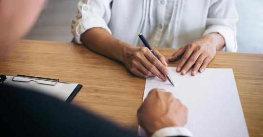 An attorney pointing on a piece of paper to where a person holding a pen should sign