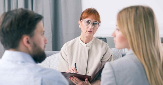 A woman sitting across from a man and another woman. She appears to be talking them through something
