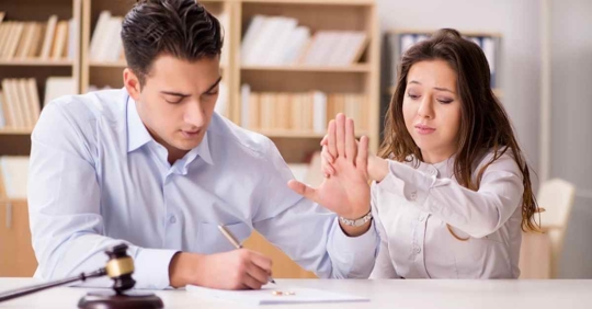 A man signing papers while a woman next to him grabs his hand and tries to stop him
