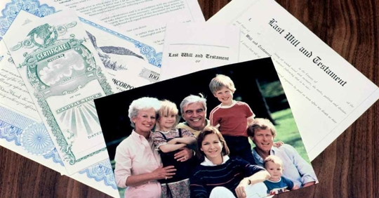 A picture of a family made up of an older man, an older woman, a middle aged couple, and three young children resting on estate planning documents