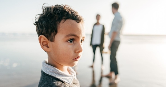 A child on the beach with his parents discussing something in the background