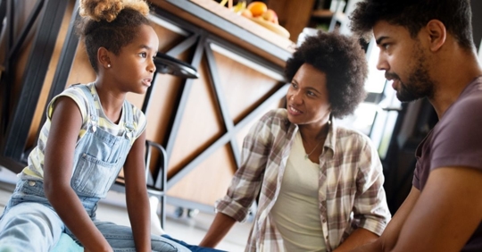two parents and child sitting on the floor having a serious conversation