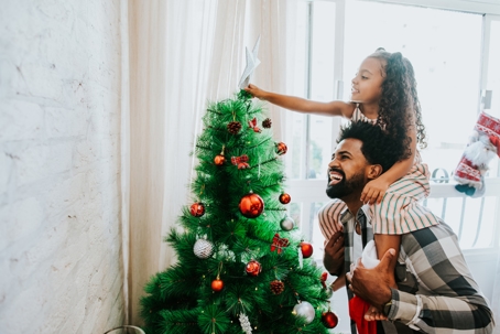 father and daughter placing star on top of Christmas tree