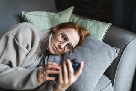 woman scrolling on her phone while lying on the couch